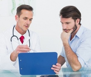 Male doctor discussing reports with patient at desk in medical office